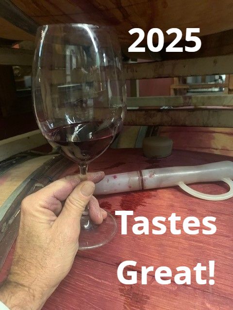 A hand swirling a glass of red wine over the barrels. Text on the photo reads 2025 Tastes Great!