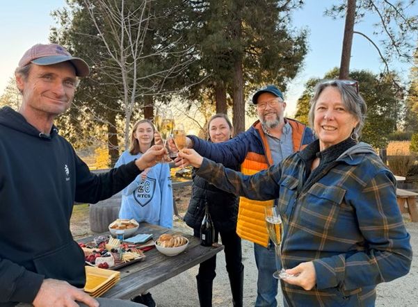 Six people raising their glasses in a toast at an outdoor table