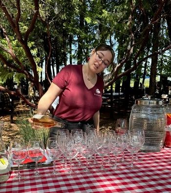Tessa Bush setting out wine glasses on a checkered tablecloth under the trees